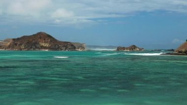 Lombok, Endonezya 'daki Tanjung Aan plajının gerçek, insansız hava aracı görüntüsü. Su koyunun etrafı kayalıklarla çevrili. Suyun birçok mavi tonu vardır. Plajda dinlenmek için mükemmel bir gün. Güçlü dalgalar