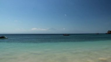 Lombok, Endonezya 'da cennet gibi bir plaj. Arka planda Rinjani volkanı varken deniz sakin. Kıyı boyunca sürüklenen renkli tekneler. Bozulmamış, gizli mücevher.