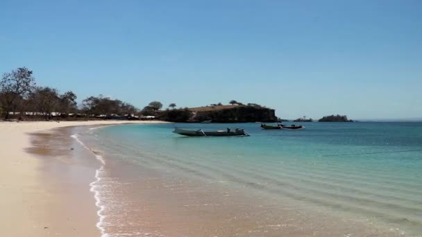 インドネシアのロンボク島にある牧歌的なピンクビーチ。海、青の多くの色合いで輝いて落ち着いている。海岸に沿って漂流カラフルなボートの多く。手付かずの隠された宝石。後ろには大きなヘッドランドがあります — ストック動画