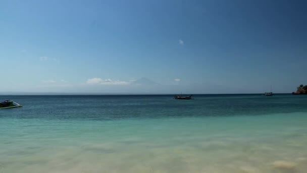 Μια ειδυλλιακή παραλία στο Λόμποκ της Ινδονησίας. Θάλασσα είναι ήρεμη με ηφαίστειο Rinjani στο παρασκήνιο. Πολύχρωμα σκάφη που πλέουν κατά μήκος της ακτής. Άσπιλο, κρυμμένο πετράδι — Αρχείο Βίντεο