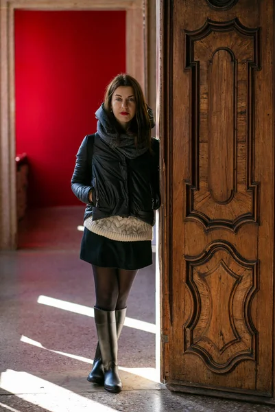 身穿黑色夹克和黑色高跟鞋的年轻黑发欧洲女人靠着一座老房子的墙壁站着 — 图库照片
