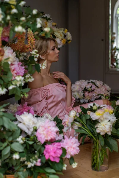 ピンク色のドレスを着た美しい若い女性が花でいっぱいの部屋に座っている ストック写真
