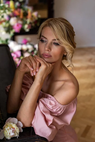 素っ裸の肩を持つ美しいピンクのドレスの悲しい若い女性が思慮深く部屋に座っている ロイヤリティフリーのストック写真