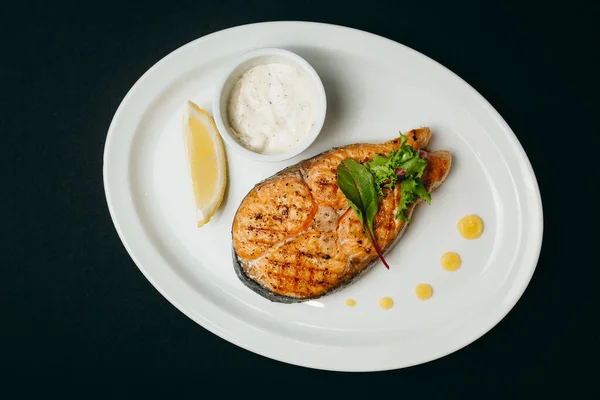 Appetizing grilled salmon steak with sauce and a piece of lemon