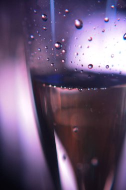 Koyu mor renklerde arka ışıkta şampanya ile şarap kadehi cam yüzeyinde Damla
