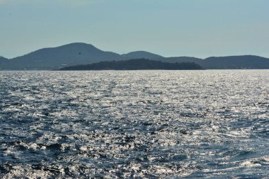 Ufukta dalgalanan dalgalar ve gölge tepeler ile berrak mavi deniz suları