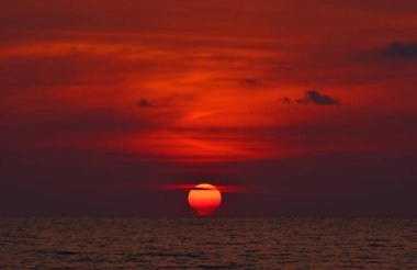 Ufukta dalgalanan denize batan güneşin son derece parlak ve koyu kırmızı manzara görünümü