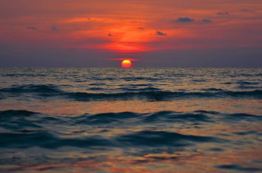 Ufukta dalgalı denize batan güneşin son derece parlak ve koyu kırmızı manzara görünümü