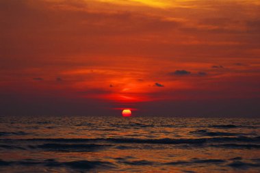 Ufukta dalgalı denize batan güneşin son derece parlak ve koyu kırmızı manzara görünümü