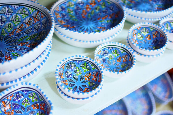 Unique handmade tracery oriental traditional pottery crockery plates made of natural clay painted to a multicolored ornament,and glazed on a market shelf set in a row diagonal top view close up