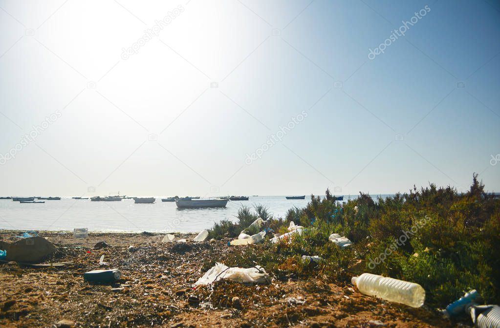 Dirty landscape lot of trash, garbage, empty plactic bottles on the sea beach with many boats on a sunny bright day. It shows carelessness of people and their neglect of nature pollution