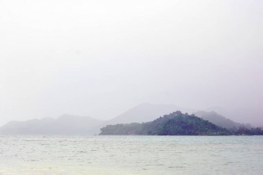 Kalın sis küçük satır dalgaları ile pürüzsüz sakin deniz yüzeyi tarafından yağmurlu sisli ada tepeler. Tayland mucize ve gizemli ortamda güzel Asya okyanus adaları manzara arka plan görünümü