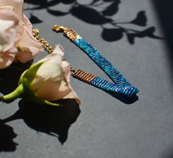 闪闪发光的珠子手工珠宝手镯在黑色背景与叶子阴影和鲜花 闪亮的蓝色和金色装饰 可调长 龙虾扣和金链 便于固定 — 图库照片