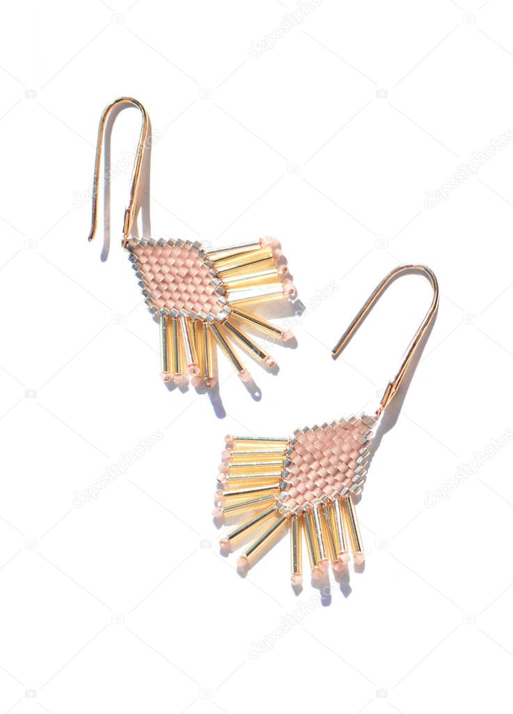 Isolated sparkling beaded handmade jewelry  earrings in art-deco style made in pastel light pink, silver and gold colors on white background. Very shiny and lovely decoration to every event. Top view 