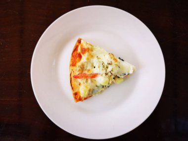 parça pizza ile koyu kahverengi masa arka plan beyaz çanak üzerinde. boşaltmak.