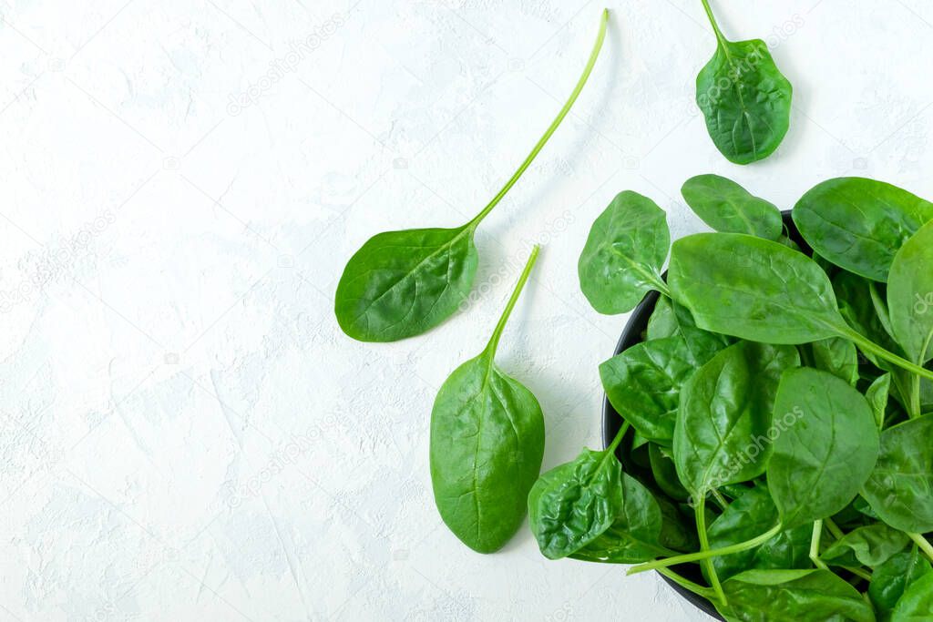 Fresh spinach leaves in a black bowl on a light surface. Fresh greens. Vegetarianism, healthy eating concept. Horizontal orientation, selective focus. View from above, copy space.