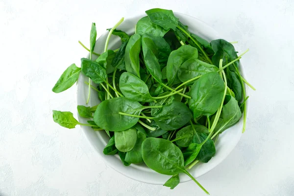 Fresh spinach leaves in a white bowl and on a light surface — Stock Photo, Image