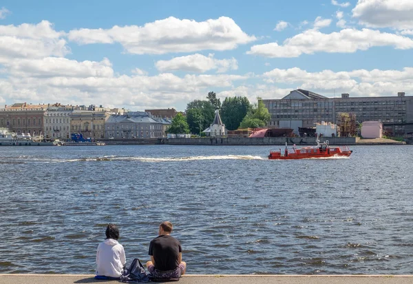 St. Petersburg, Rusya. 21 Haziran 2020. Neva Nehri manzarası, karşı kıyıda. Genç bir çift setin kenarında oturur ve dinlenir. Yatay yönelim, seçici odak.