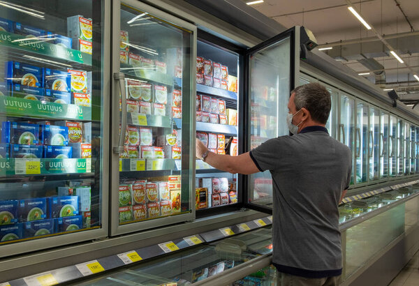 Мужчина средних лет в медицинской маске берет продукт из холодильной витрины в магазине
.