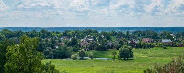 Ilıman bir kıta ikliminde, evler, ağaçlar, yeşil çimenler ve bir göleti olan kırsal bir yaz manzarası. Pankart. Yatay yönelim, seçici odak.