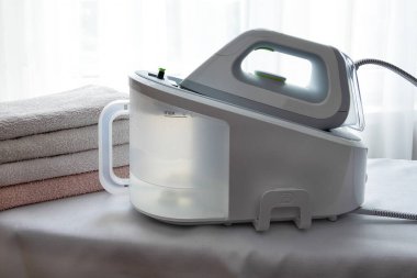 Buhar jeneratörlü bir elektrikli ütü ve hafif bir yüzeyde ütülenmiş havlular. Ekonomi, ütü iç çamaşırı. Yatay yönelim, seçici odak.