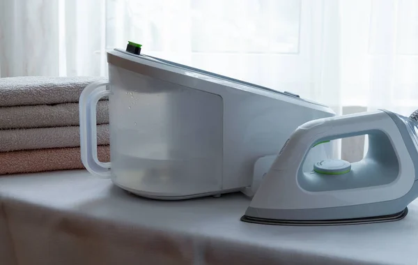 An electric iron with a steam generator and a stack of ironed towels on a light surface. Economics, ironing underwear. Horizontal orientation, selective focus.