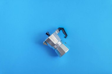 The aluminum geyser coffee maker lies on its side in the center of the blue background. View from above. Horizontal orientation, selective focus. clipart