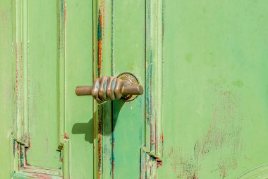 Eski kapının eski kolu, bronzdan yapılmış, yumrukla sıkılmış bir el şeklinde. Yatay yönelim, seçici odak.