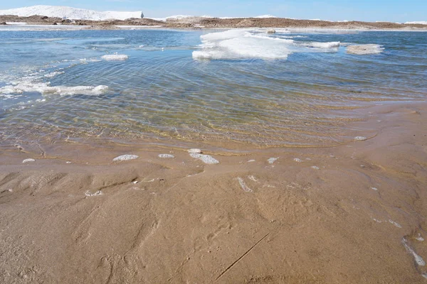 春日的湖岸 水中有冰雪 背景是蓝天 前景是海滩 — 图库照片