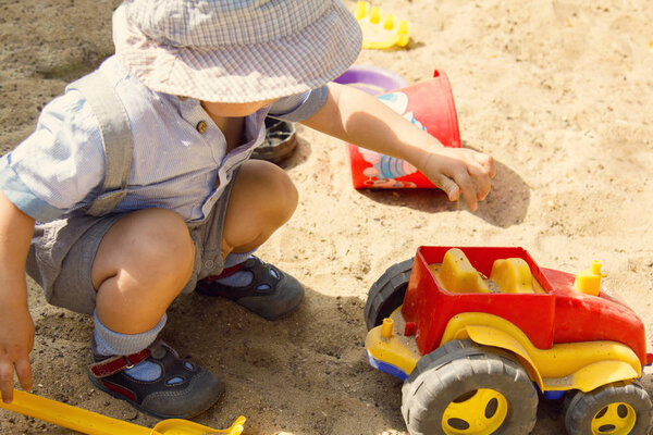 A little boy is plaing with red toy car in a sand