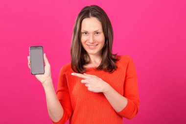 Güzel esmer kadın Smartphone'da onu el ayakta pembe bir arka plan üzerinde gösterir.