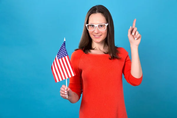 Beautiful brunette woman with the flag of the united states of america in hands on a blue background. Young woman with a flag shows a up.