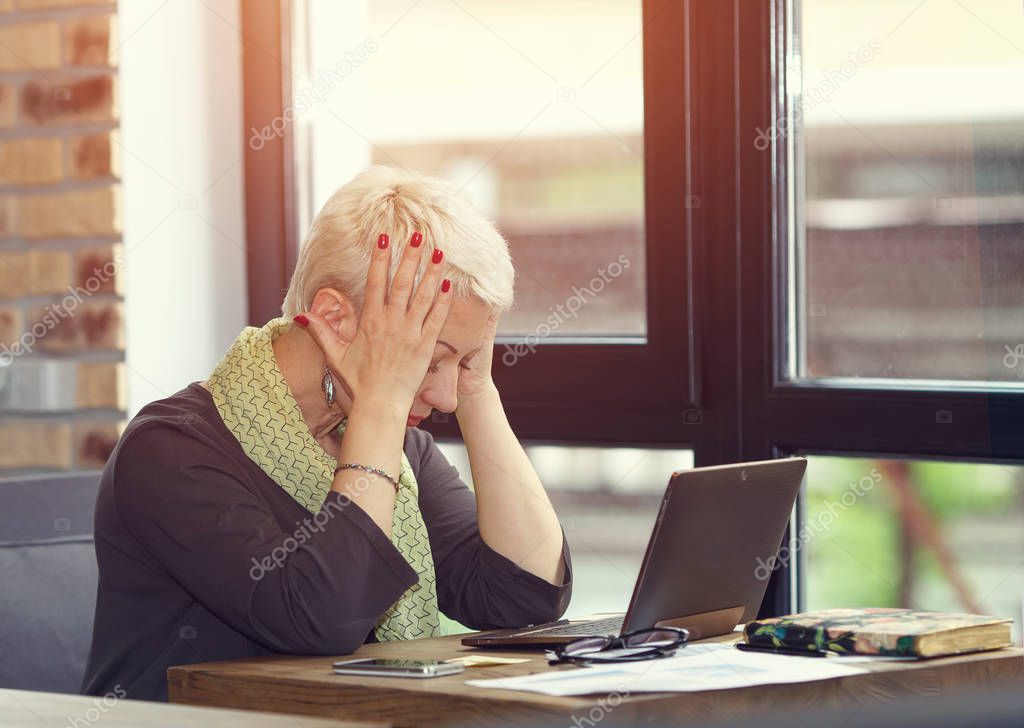 Adult woman thinking about to complete work task. Tired woman working at office desk in front of laptop suffering from chronic daily headaches from computer. Frustrated woman.