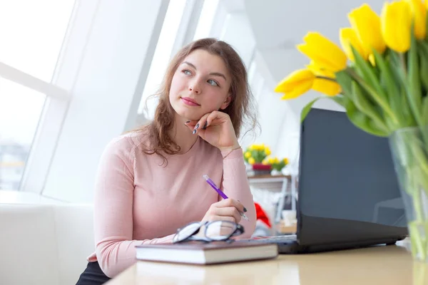 年轻女子坐在桌边学习 在办公室与新的启动项目工作的妇女 桌面上的一束黄色郁金香花 — 图库照片