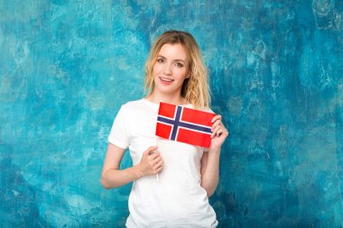 Norveç bayrağı mavi duvar arka plan üzerinde mutlu sarışın kadınla. İskandinav kadın.