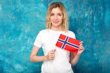 Norveç bayrağı mavi duvar arka plan üzerinde mutlu sarışın kadınla. İskandinav kadın.
