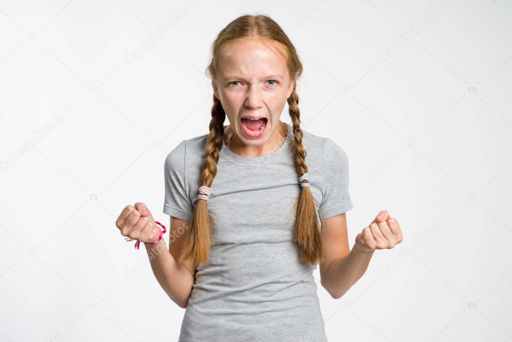 Teenage aggression. The girl screams standing on a gray background.