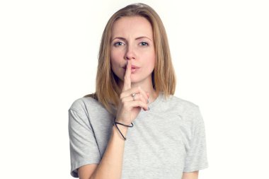 Kadın tutmak gizli. Jest şşş işaret parmağı ile gösterilen ağız dudaklar üzerinde kız. Gri t-shirt hafif bir arka plan üzerine genç bir kadın portresi.