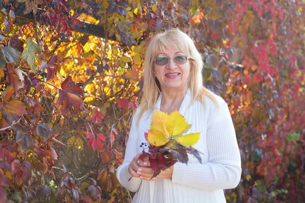 Olgun kadın sonbahar park arka plan üzerinde. 60 yaşındaki kadın kıdemli.