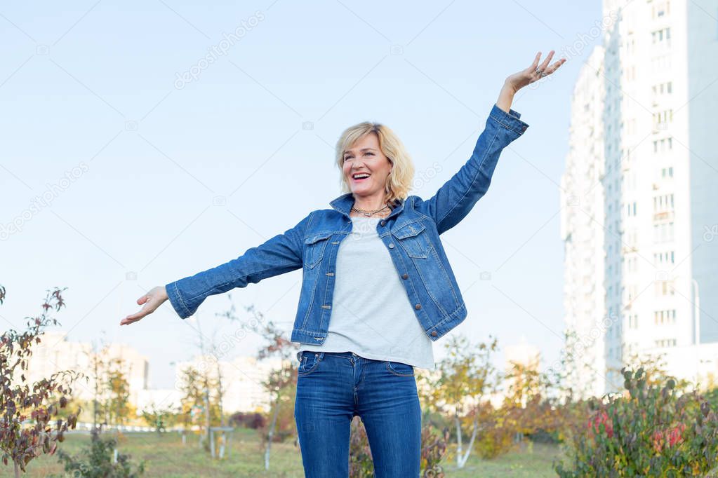 Happy mature woman on the blue sky background. Beautiful adult woman enjoying and happy - freedom concept. Second youth.