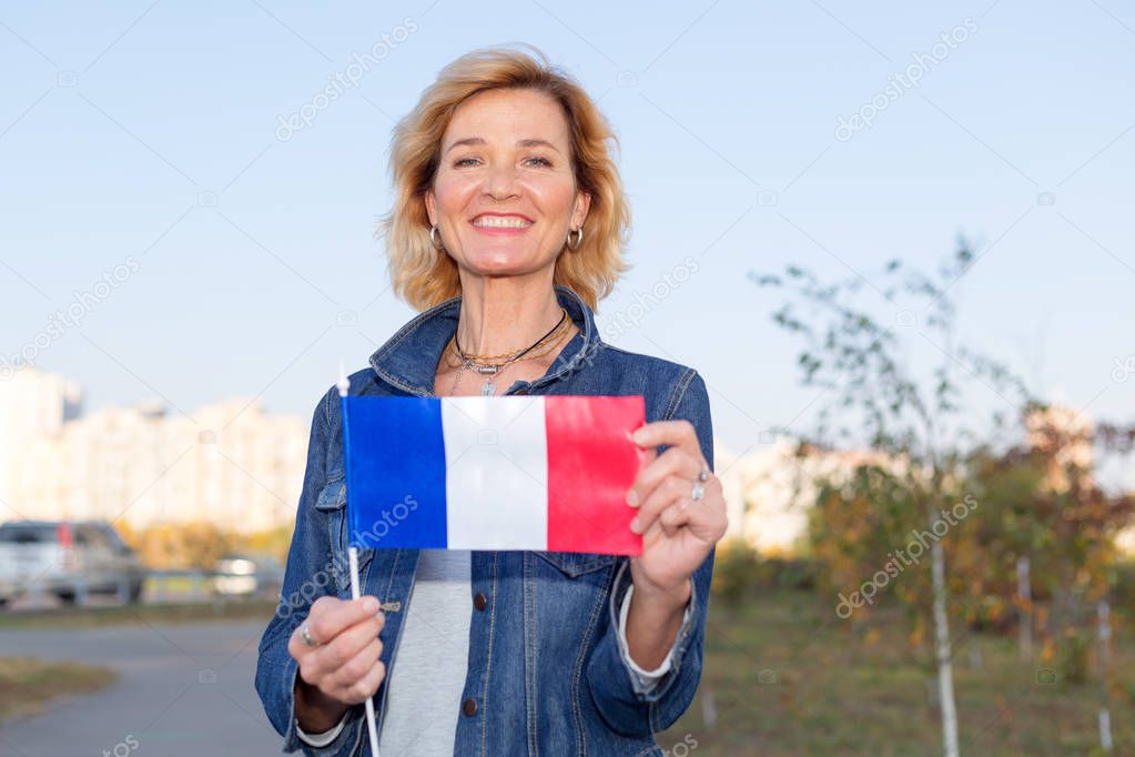 Mature woman with France flag standing against city and blue sky.