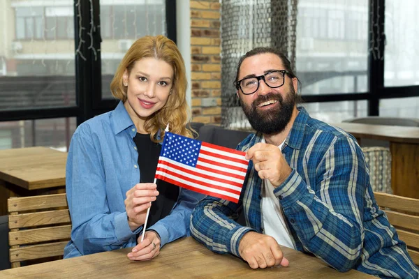 Man and woman with the flag of the USA sitting indoors at a table. A happy couple of Americans.