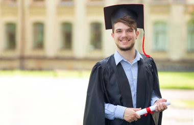 Erkek mezunu üniversite arka plan üzerinde bir diploma ile manto portresi. Mezuniyet günü, eğitim kavramı.