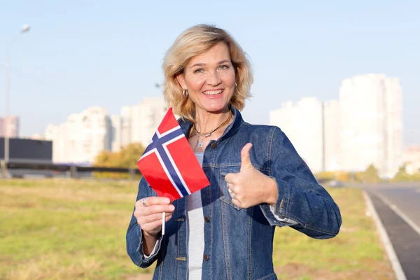 愉快的成熟的妇女与挪威的旗子显示站在城市街道和蓝天的背景下 — 图库照片
