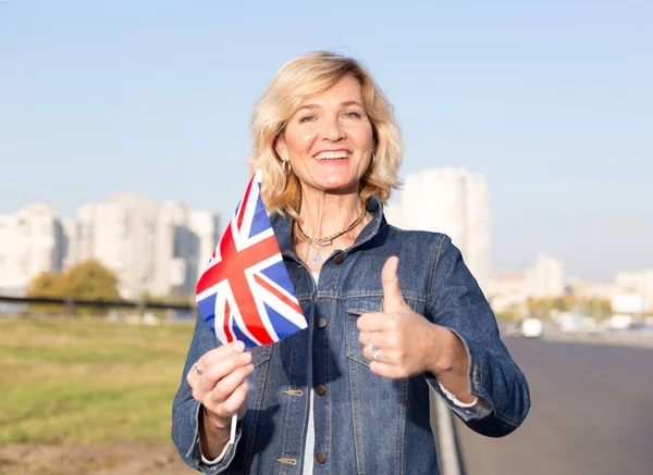 成熟的愉快的妇女与英国的旗子反对蓝天和城市 — 图库照片