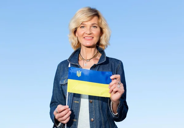 Mature woman with the flag of Ukraine on the blue sky background.
