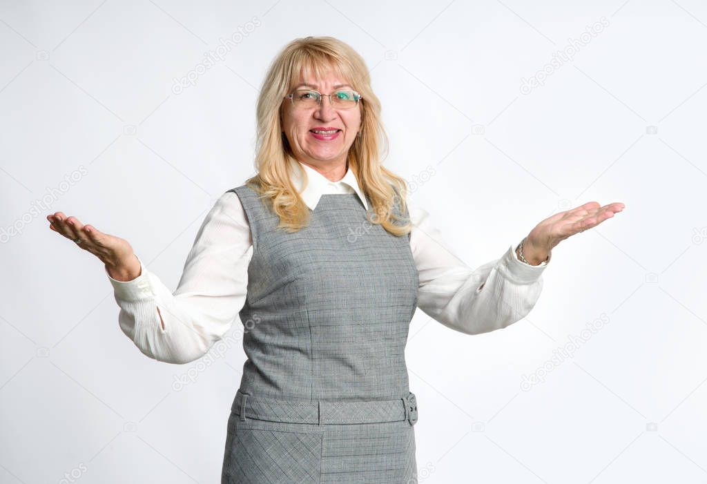 Mature woman shows her hands in different directions, standing on a gray background. Successful senior woman. Teacher.