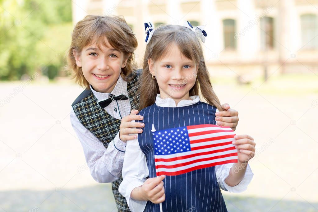 Schoolchildren boy and girl with the flag of the United States of America in their hands against the background of the college. Training in the USA.