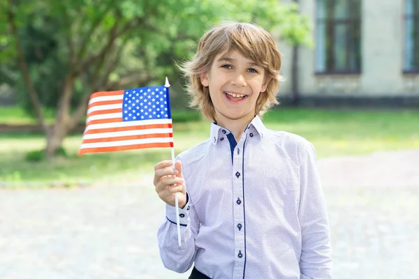 Schoolboy with the flag of the United States of America in their hands against the background of the college. Training in the USA. Study abroad. School holidays in the US.