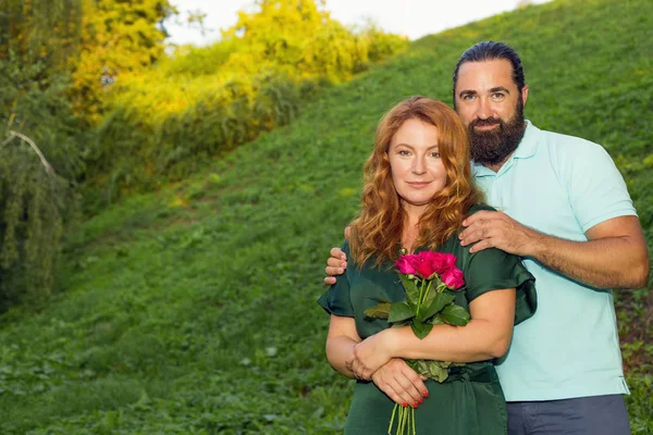 緑の自然の背景に恋に幸せな中年のカップル 男はその女性にバラの花束を贈った — ストック写真